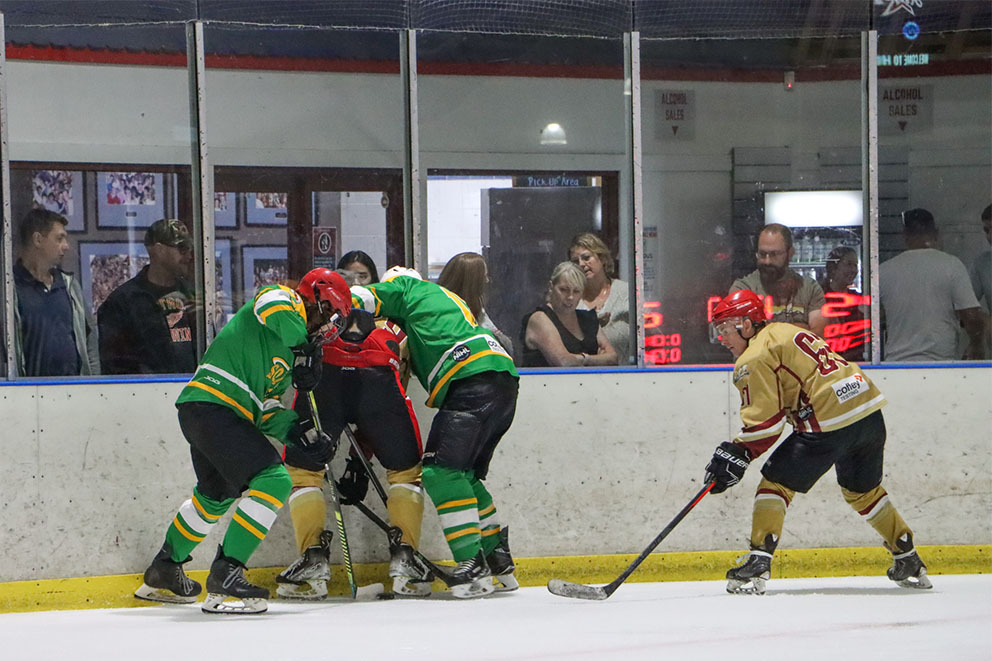 Astros and Sonics players battle for the puck against the boards in a Newcastle Ice Hockey League game while fans look on from the glass.