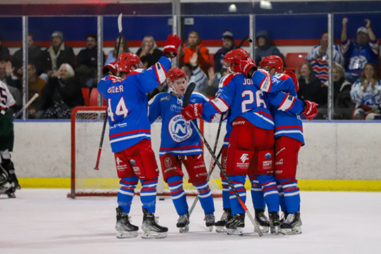 The Newcastle Northstars celebrate the scoring of a goal, with all five skaters hugging in a circle.