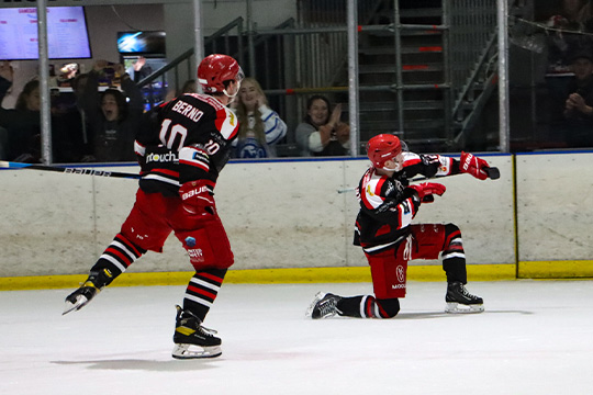 A Newcastle Northstars forward celebrates a goal with the 'Archer' celly, sliding on the ice on his shin, while Daniel Berno skates to join him in the celebration.