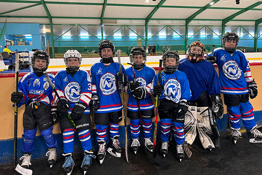 Newcastle Northstars junior representative players stand by the boards of a rink before a game.